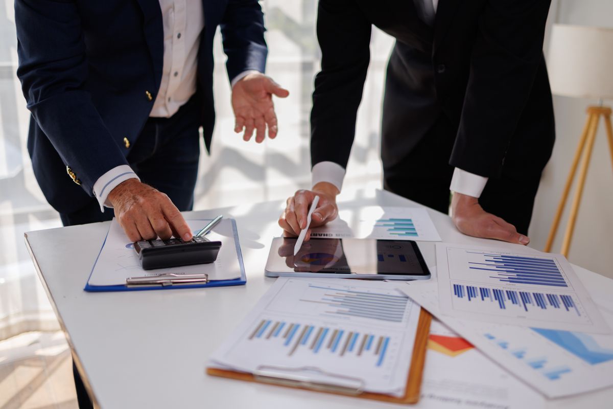 Two men in suits discussing data on tablet